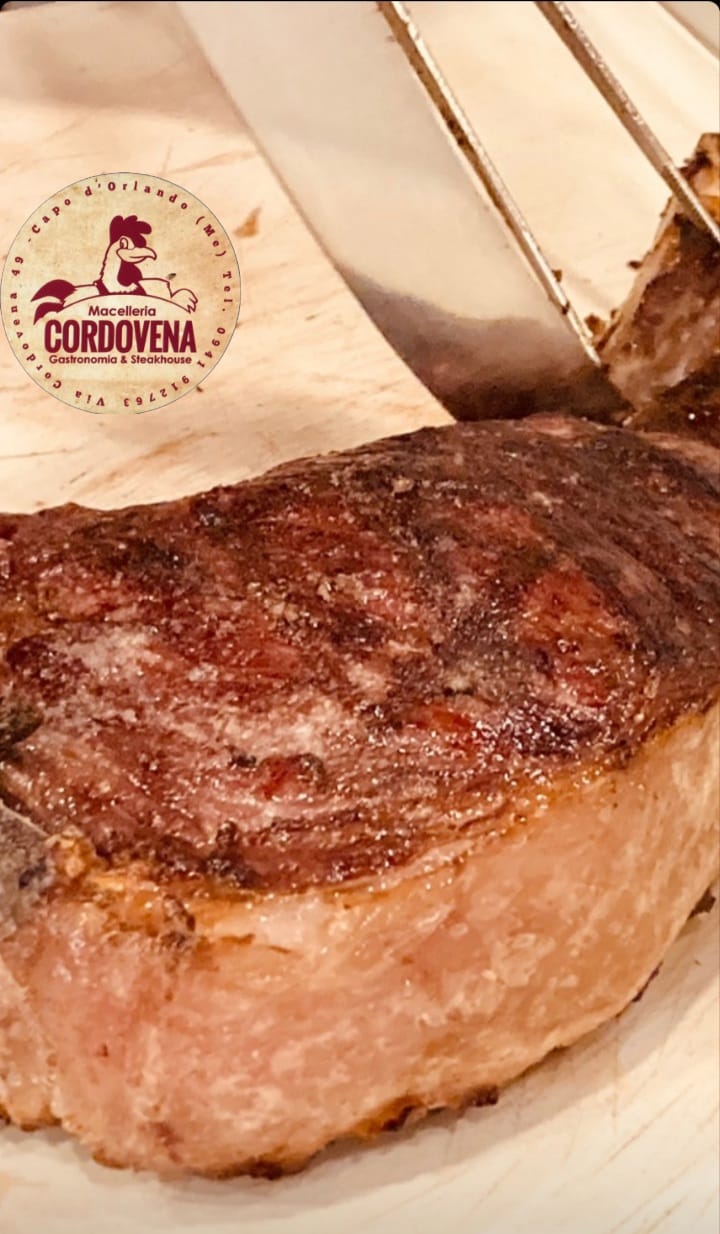 Bistecca scottata su un tagliere di legno, con le pinze inserite. Logo