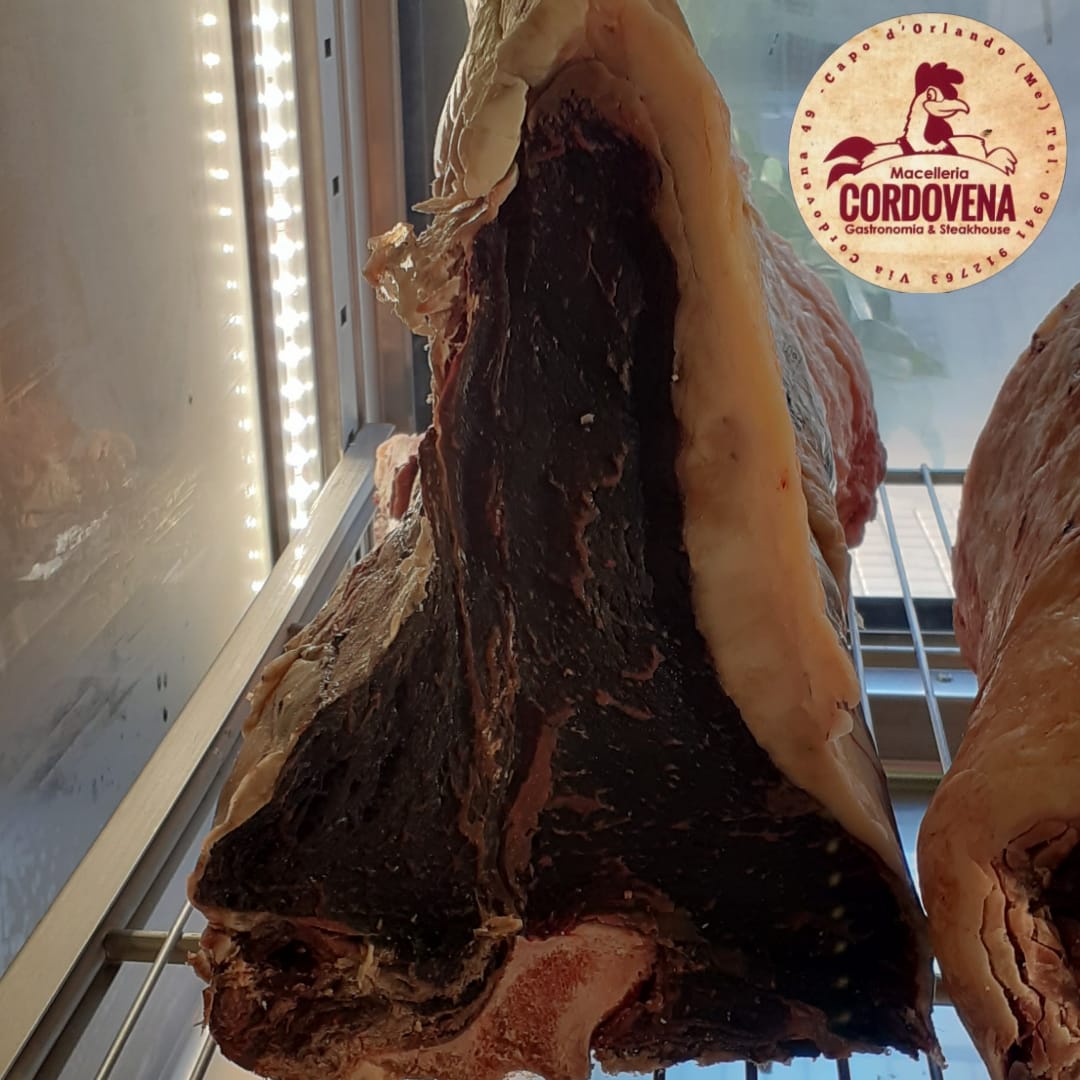Grande taglio di manzo frollato a secco con grasso spesso, appeso in una vetrina refrigerata.