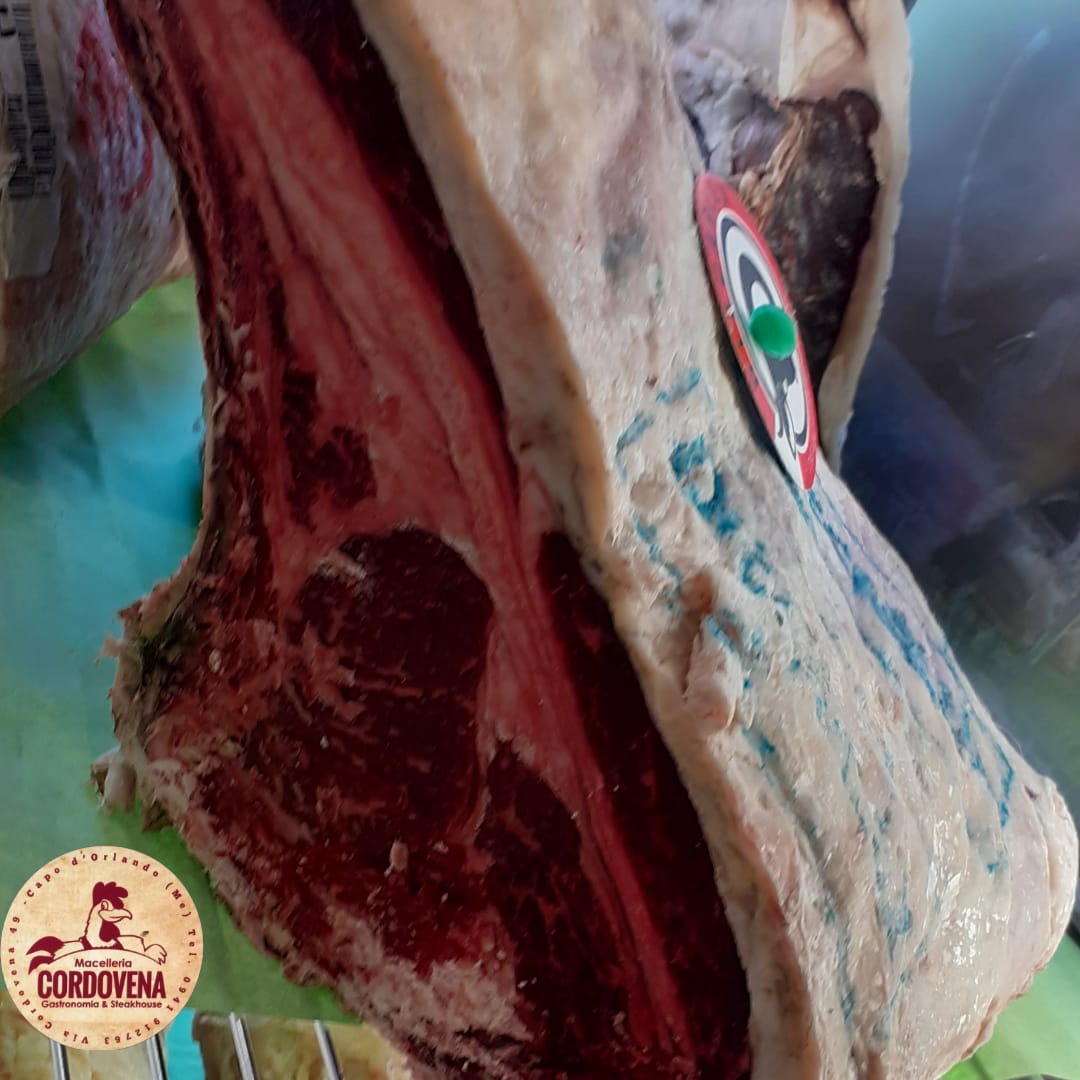 Primo piano di un grosso taglio di carne cruda con grasso bianco e muscolo rosso. È visibile un adesivo circolare.
