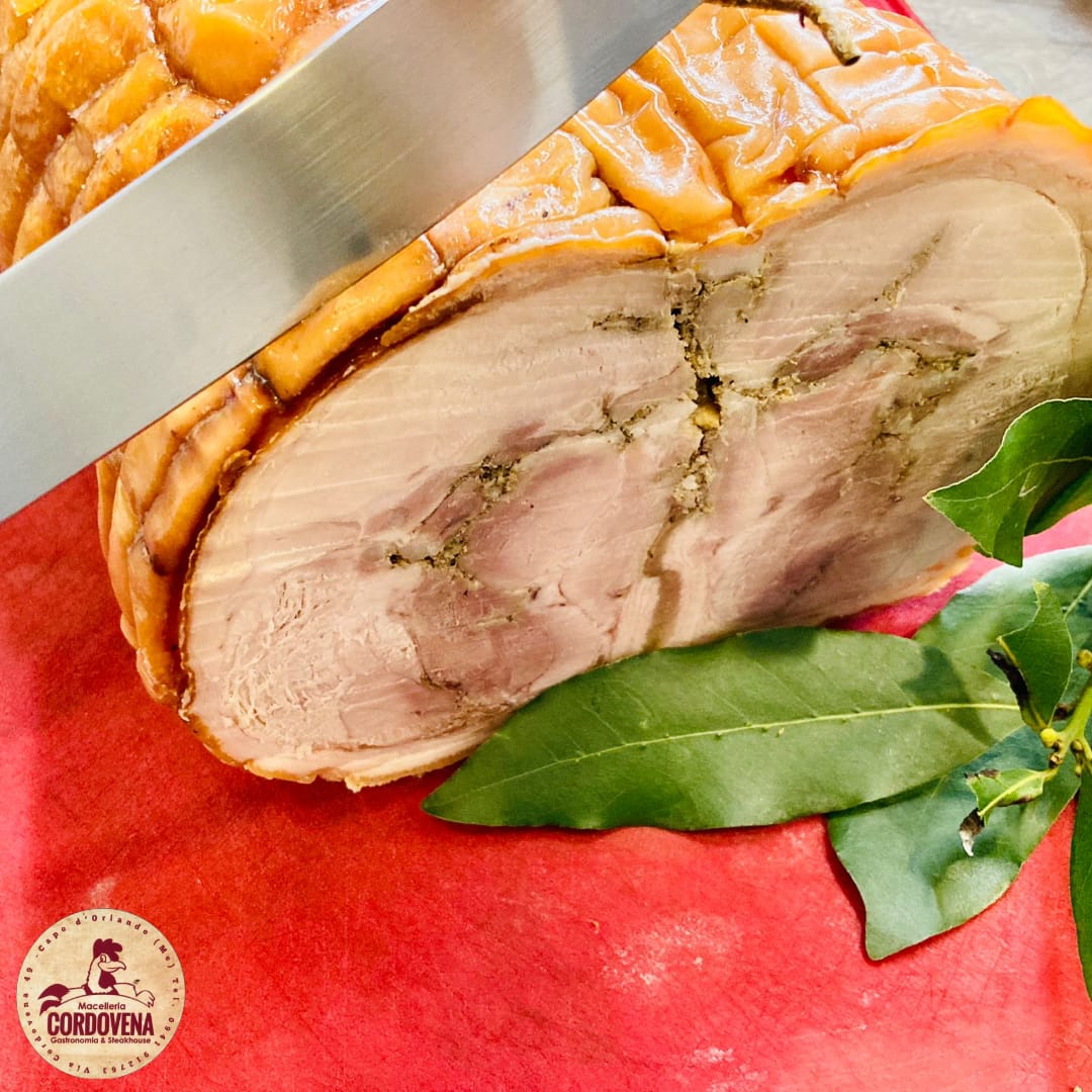 Lombo di maiale arrosto tagliato a fette, con sezione trasversale e erbe aromatiche, su una superficie rossa con foglie di alloro.