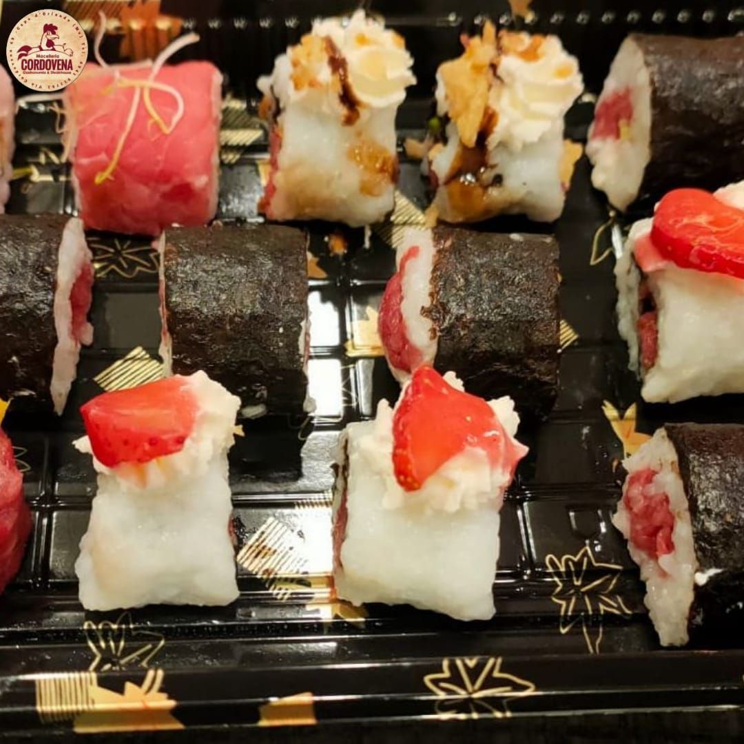Involtini di sushi serviti su un vassoio nero, alcuni guarniti con fragole, altri con noci e salse.