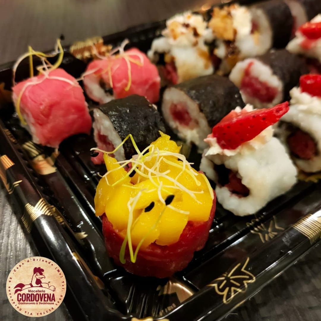 Piatto di sushi con vari tipi di involtini, alcuni dei quali guarniti con mango, tonno e salse cremose.