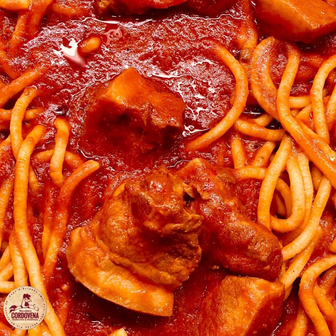 Spaghetti al sugo di pomodoro con grossi pezzi di carne, primo piano.