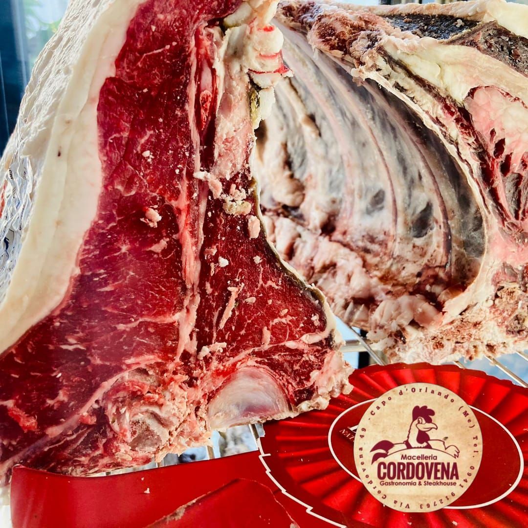 Grande bistecca cruda a T, carne rossa, grasso bianco, costole visibili, nastro rosso con logo, Cordovena.