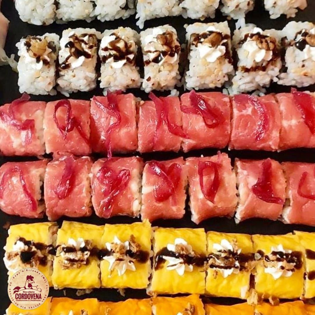 Piatto di sushi: vari involtini con condimenti e salse su una superficie nera.