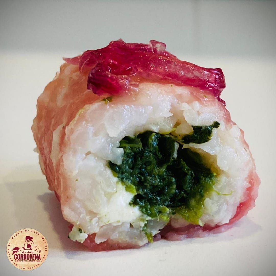 Rotolo di sushi con riso bianco, ripieno verde, avvolto in prosciutto rosa e guarnito con una guarnizione rossa.