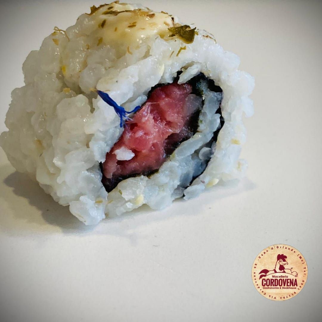 Sushi roll: tonno, riso e nori con salsa bianca ed erbe aromatiche, su fondo bianco.