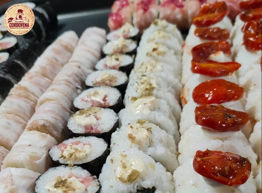 Involtini di sushi disposti su un vassoio, con vari condimenti, tra cui pomodori e panna.
