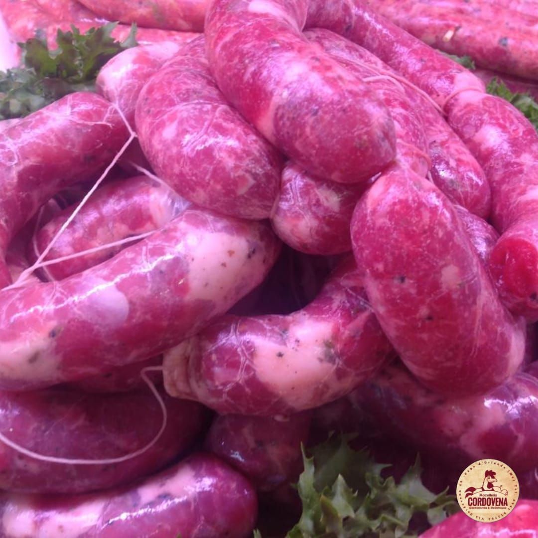 Primo piano di una pila di salsicce crude, legate insieme. Carne rosso-rosata con grasso bianco, legate con spago.