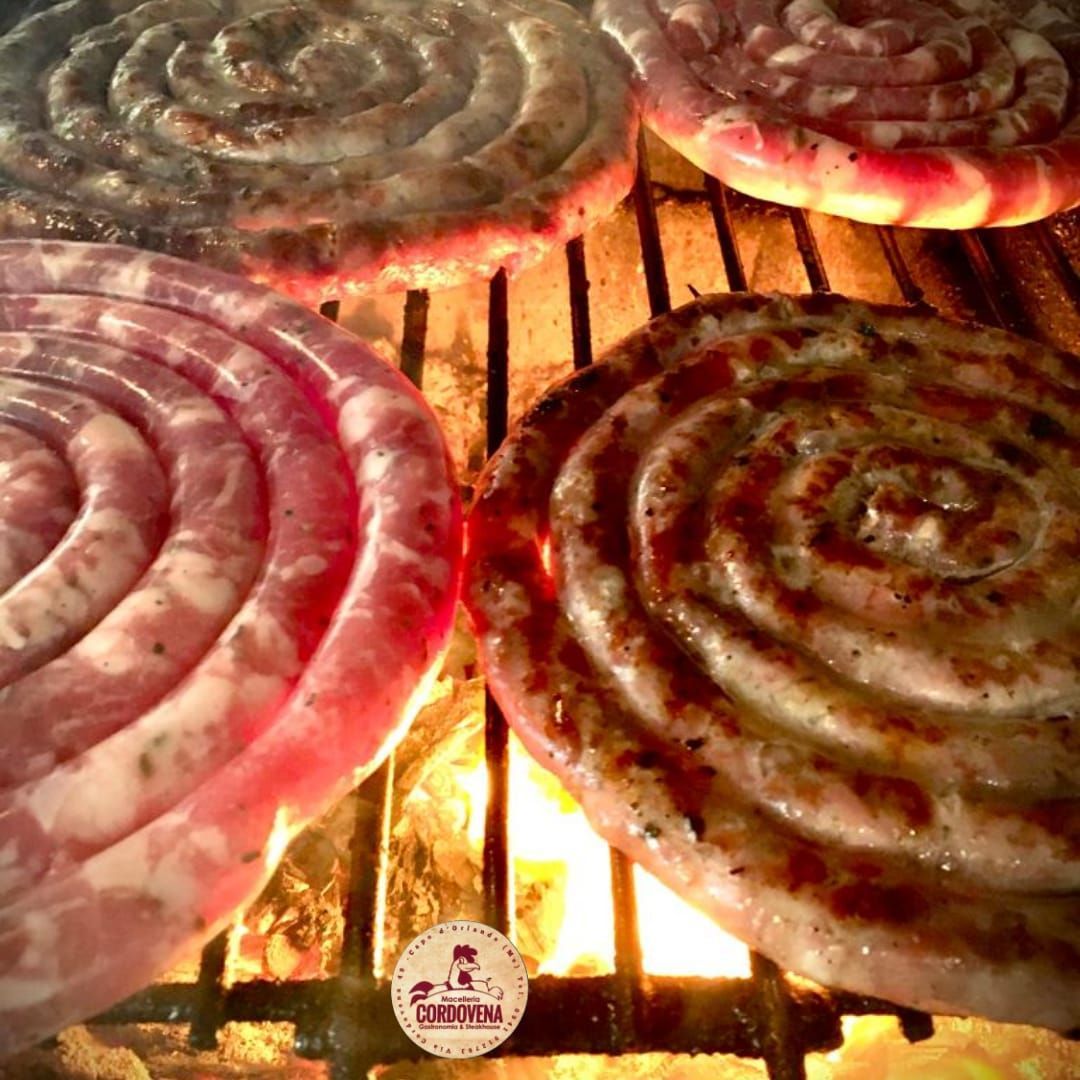 Le salsicce vengono cotte sulla fiamma, mostrando la carne rosa e dorata.