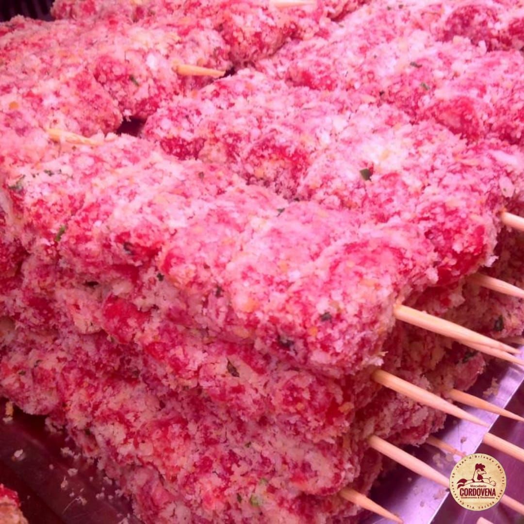 Spiedini di carne cruda infilzati, rosa e granulosi, impilati su una superficie.