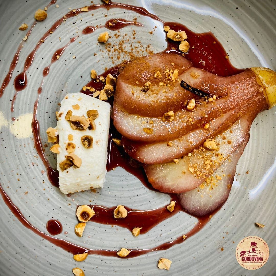 Pere a fette condite con salsa rossa e guarnite con noci, accanto a un blocco di dessert bianco, su un piatto decorato.
