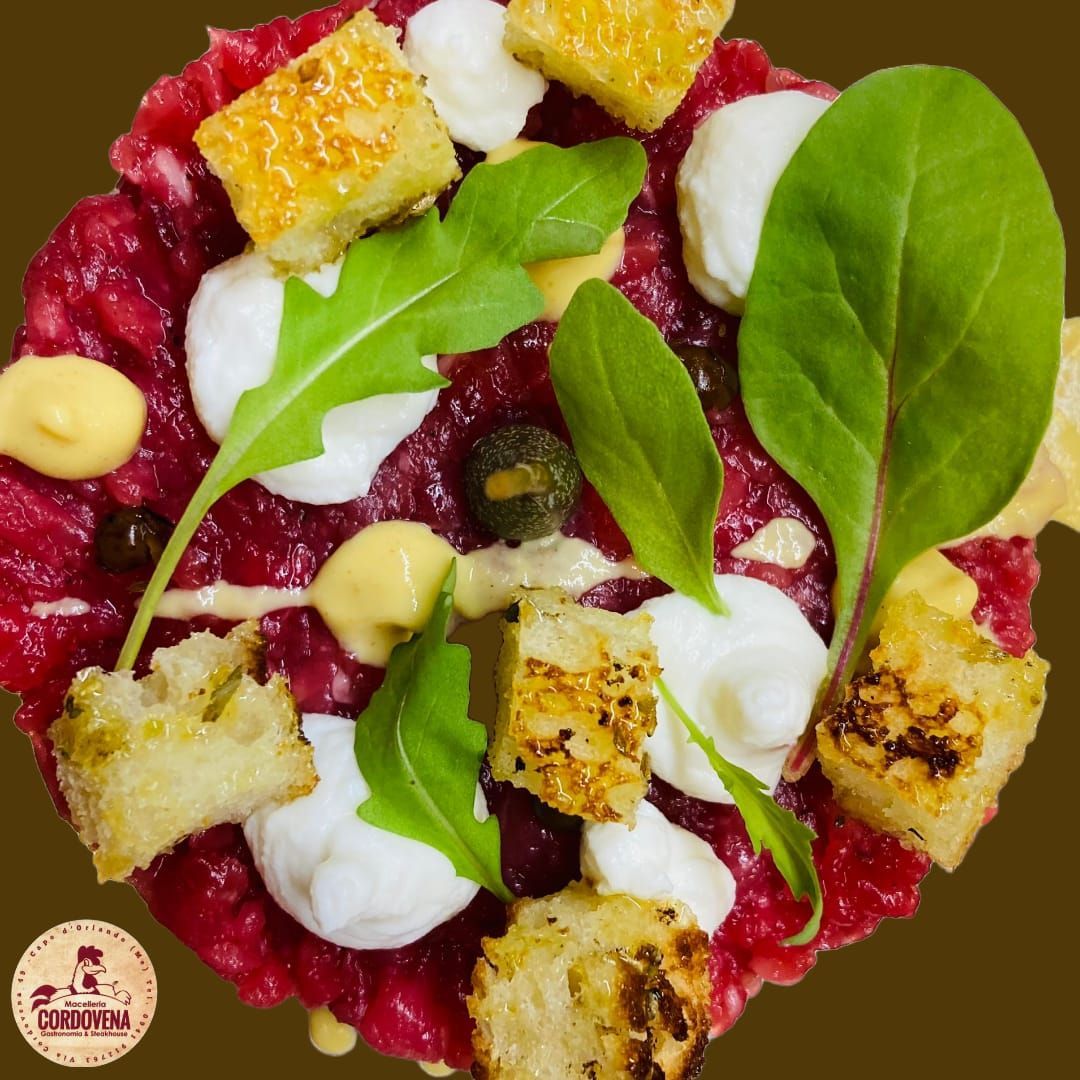 Antipasto di tartare di manzo con crostini, capperi e rucola su un piatto marrone.