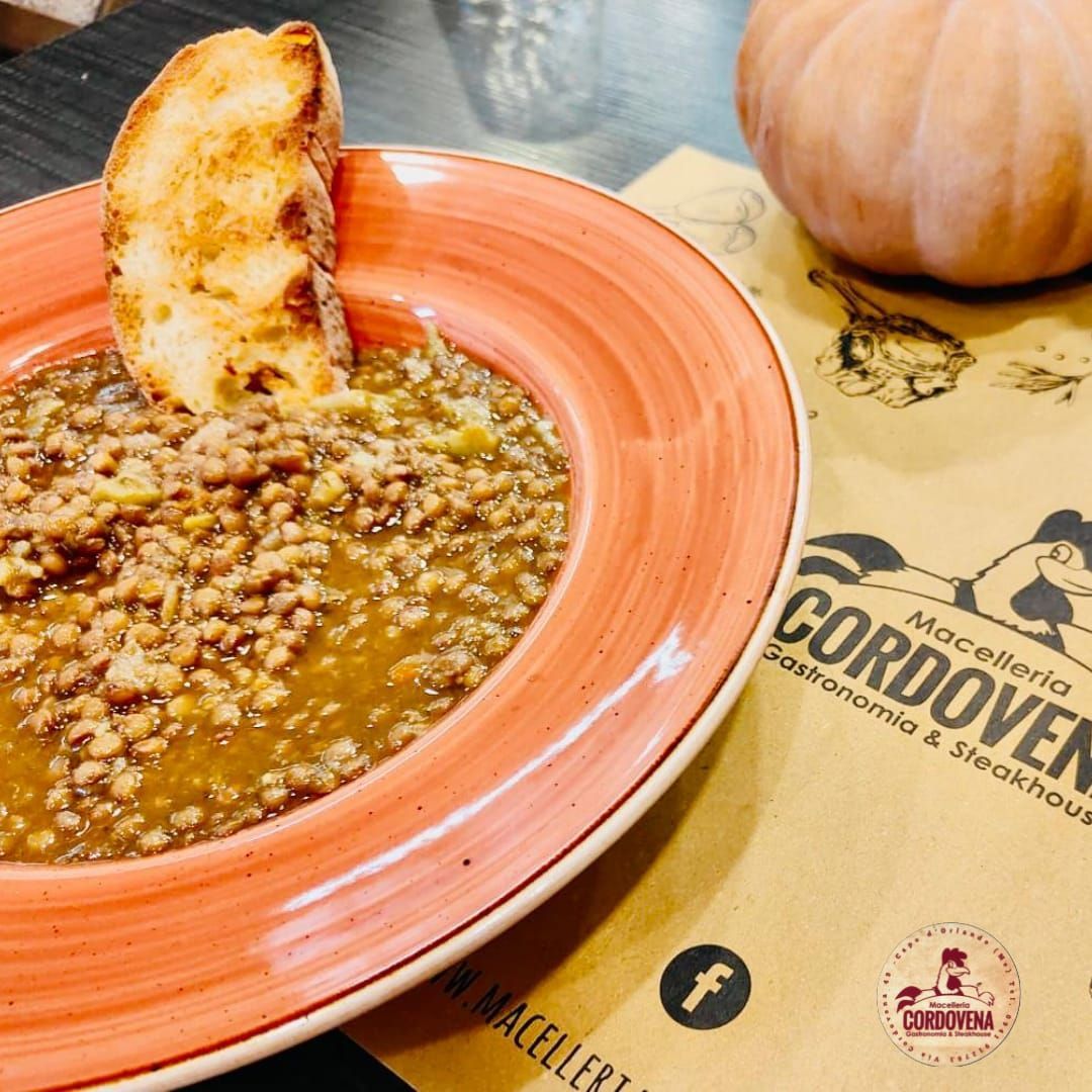 Zuppa con pane tostato in una ciotola color pesca, servita su un foglio di carta con una zucca e il logo del ristorante.