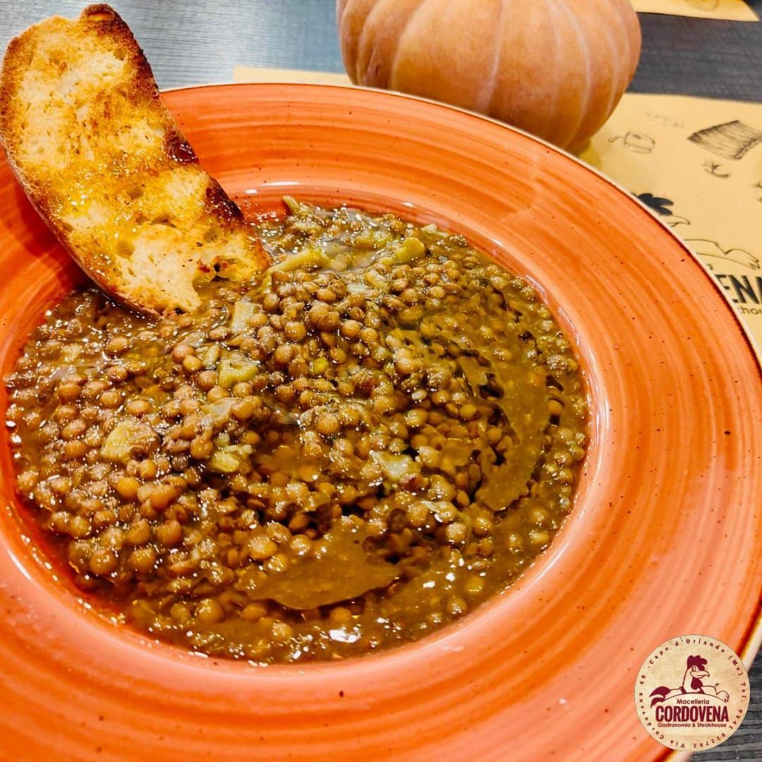 Zuppa di lenticchie marroni in una ciotola arancione con pane tostato e zucca sullo sfondo.