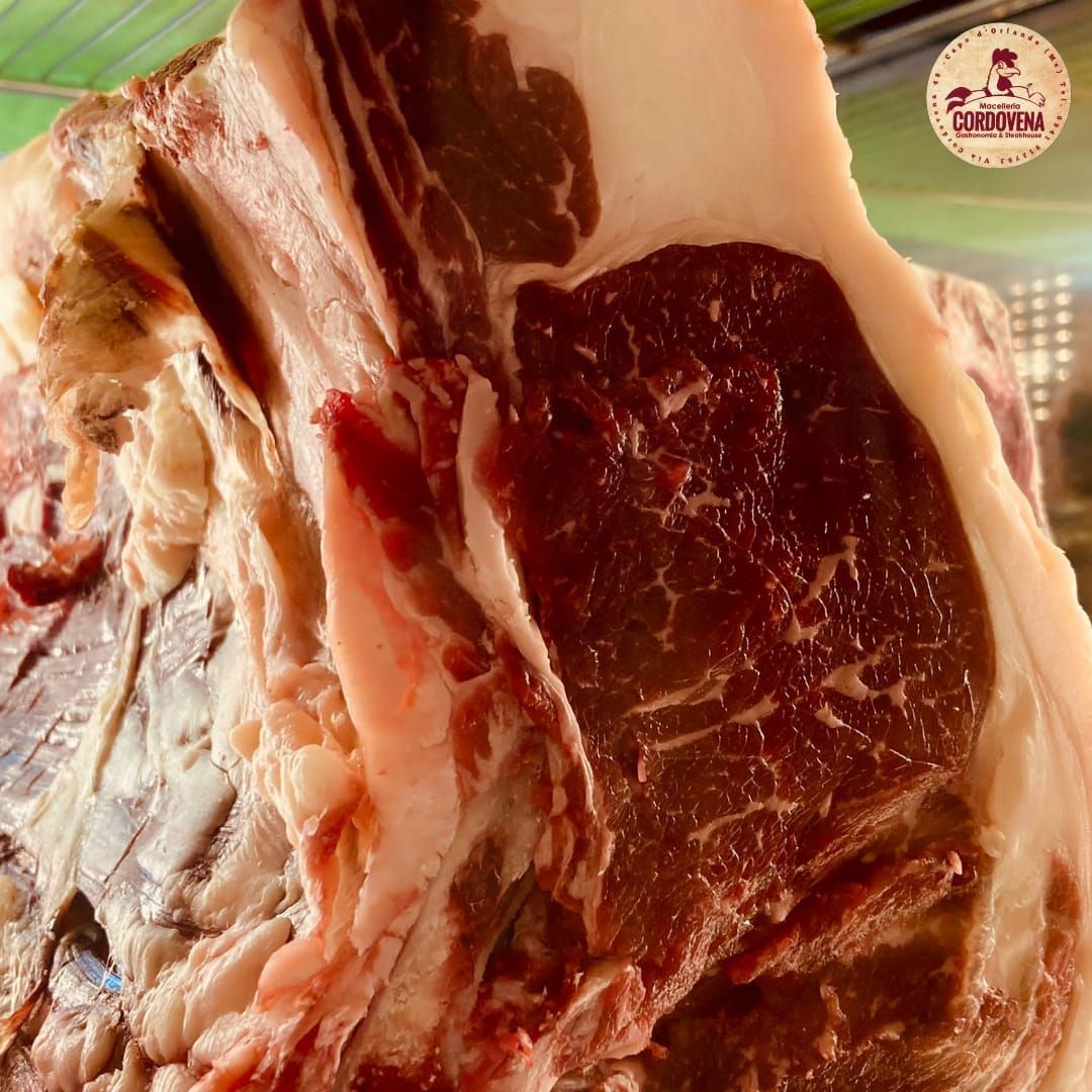 Primo piano di una bistecca T-bone cruda, tagliata spessa, con marezzature e grasso visibile.