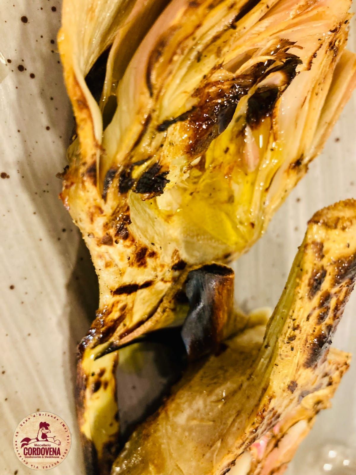 Carciofo grigliato, carbonizzato e condito con olio, in primo piano su un piatto.