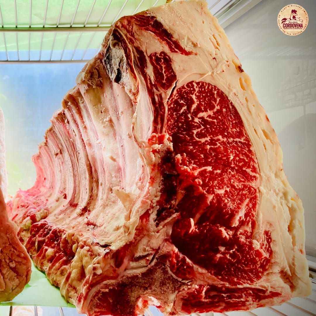 Grande bistecca di ribeye cruda, dal taglio spesso, con venature di carne rossa e ossa.