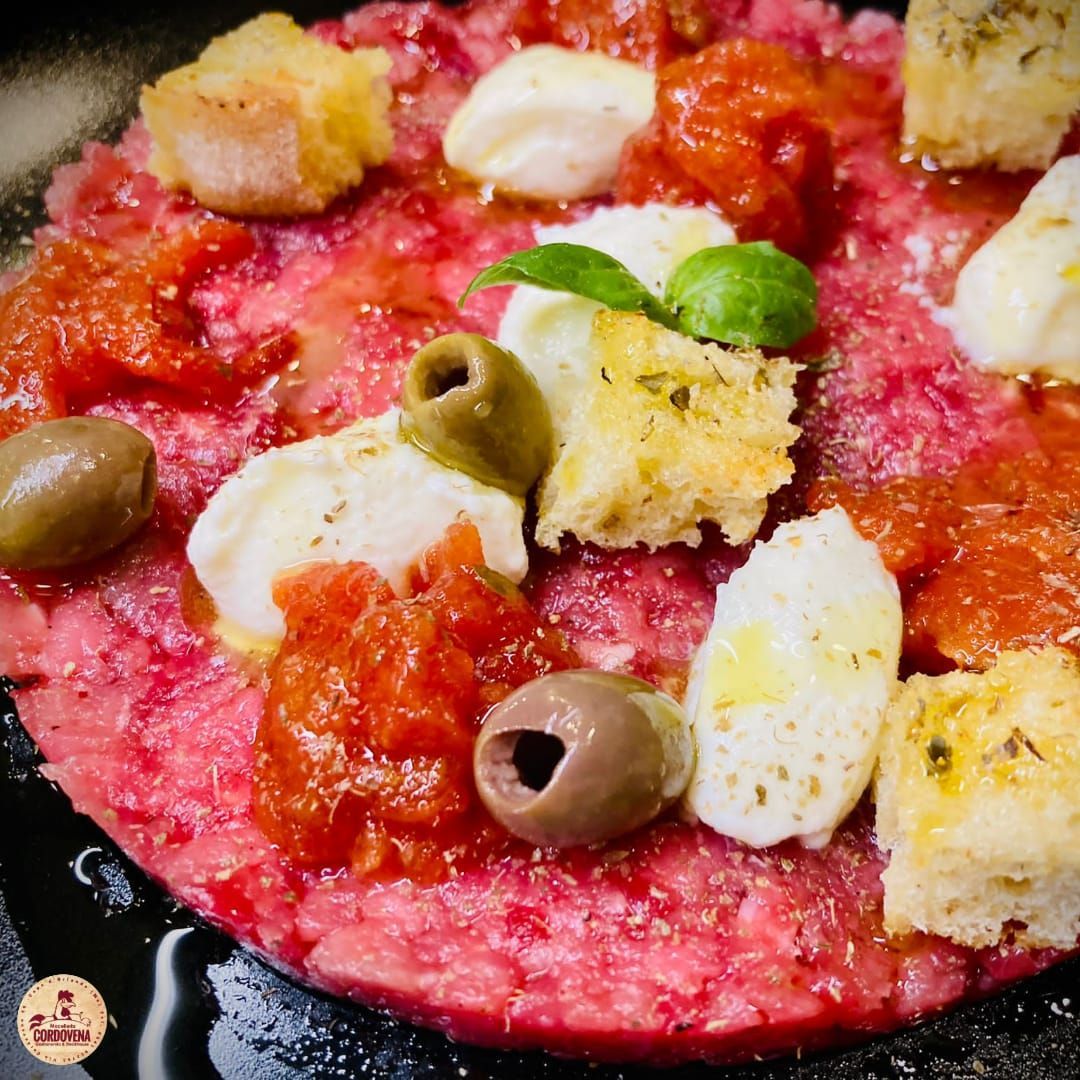 Piatto di carpaccio con pomodori, olive, mozzarella e crostini su un piatto nero.
