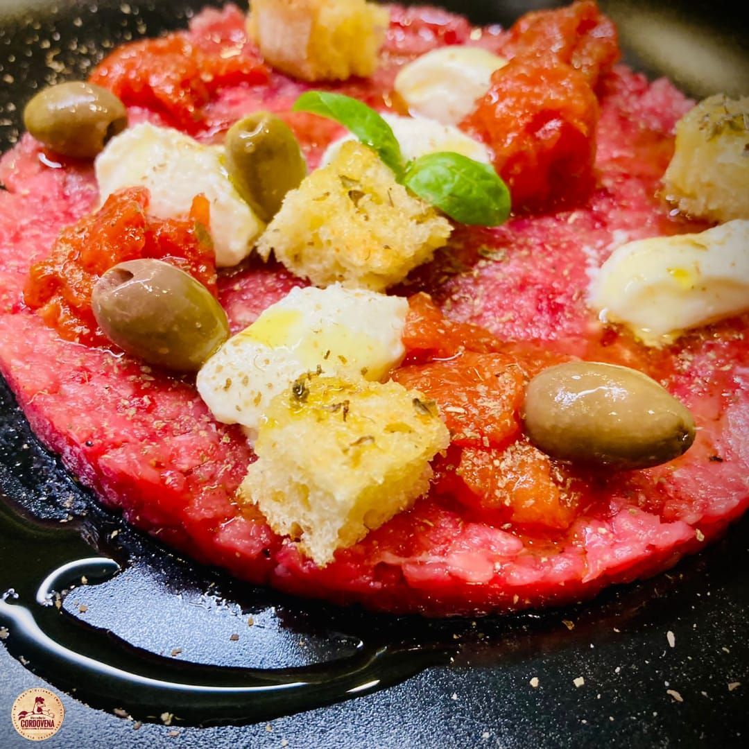 Piatto di carne macinata con pomodori, olive, cubetti di pane, mozzarella e basilico.