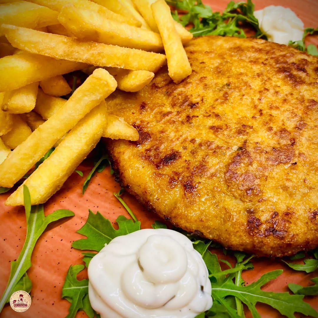 Cotoletta di pollo fritta con patatine fritte e salsa su un letto di rucola.