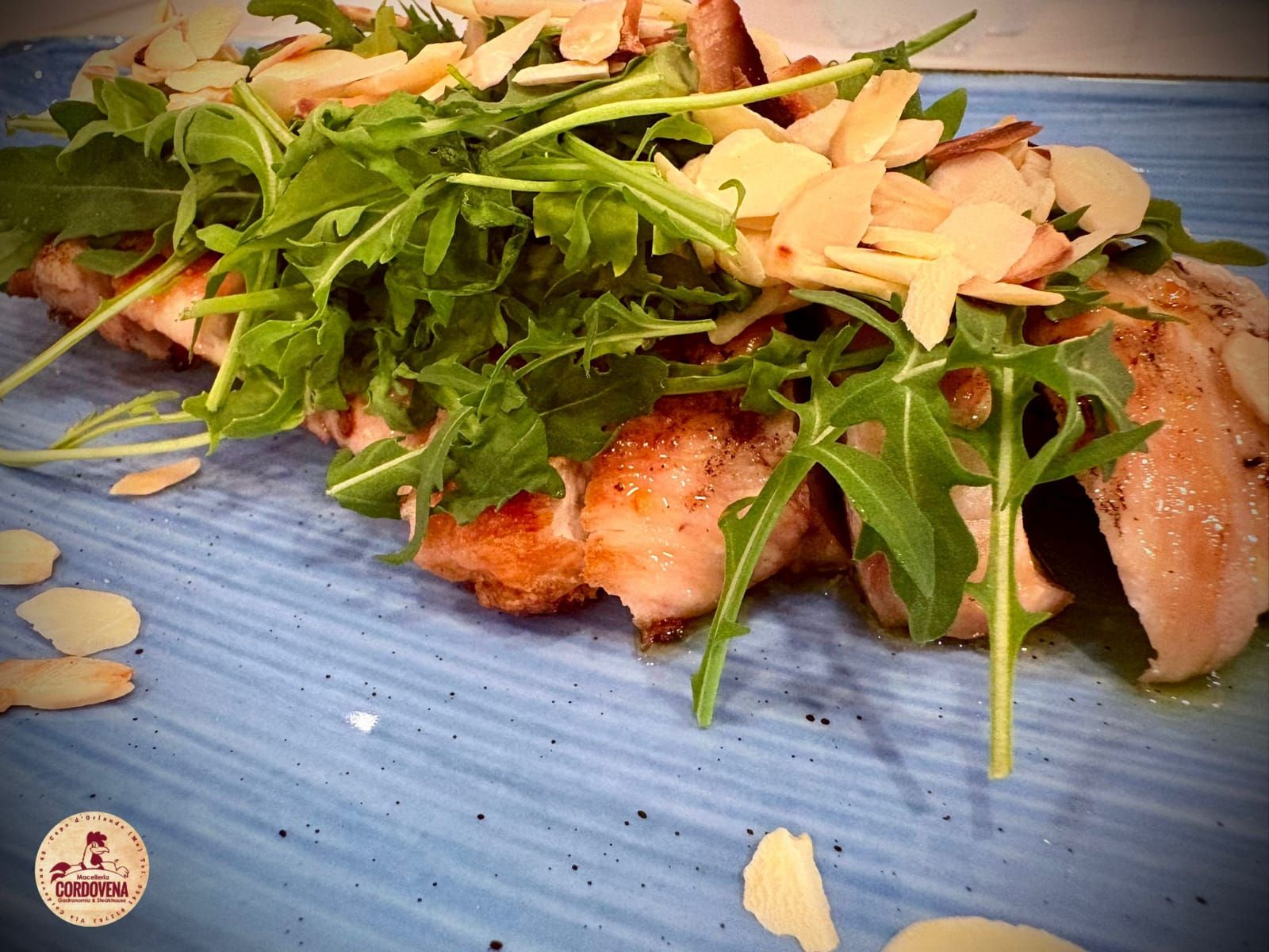 Insalata di pollo con rucola e mandorle su un piatto blu.