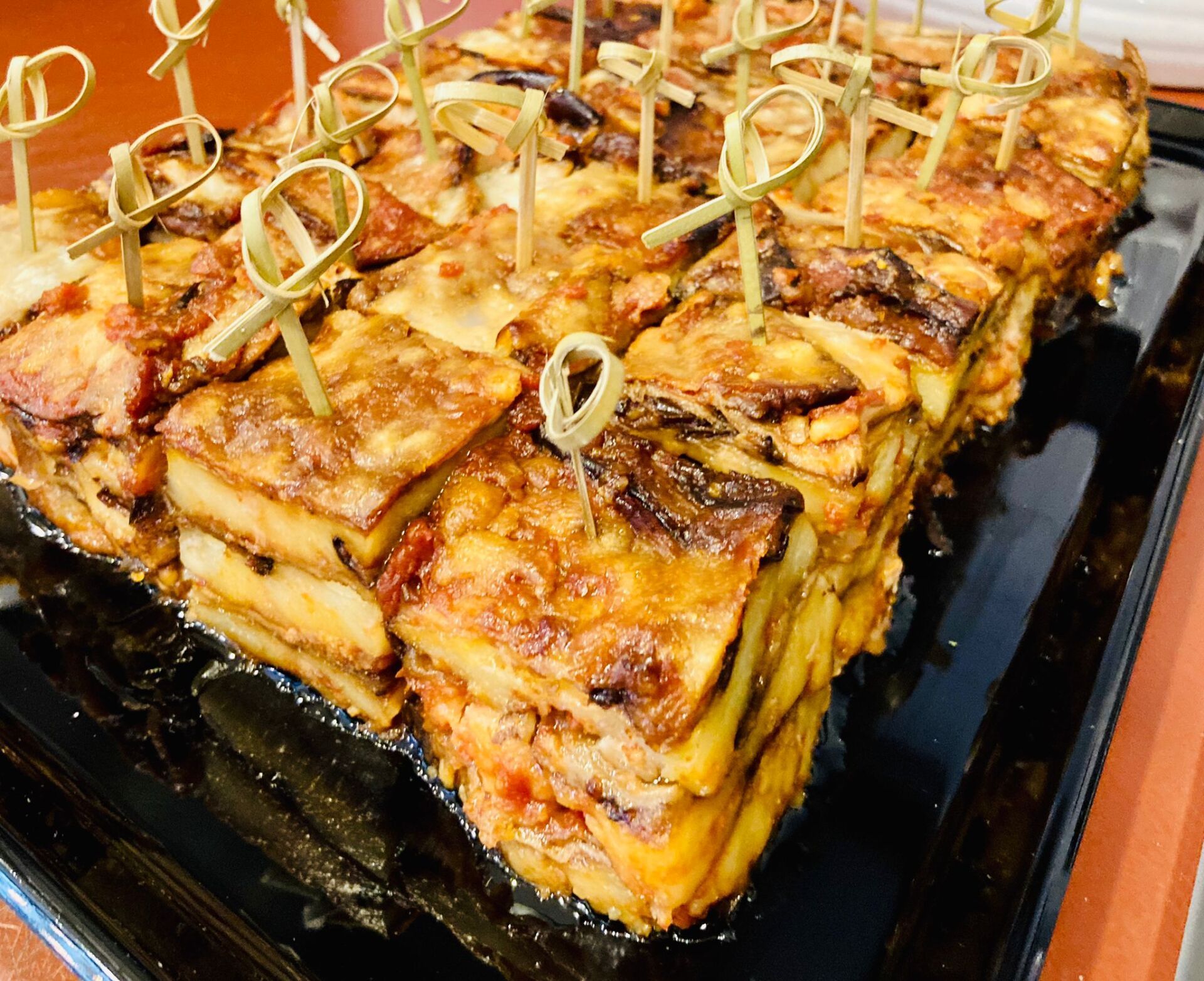 Vassoio di antipasti con strati di cibo tagliati a quadrati, ognuno sormontato da uno spiedino di bambù.