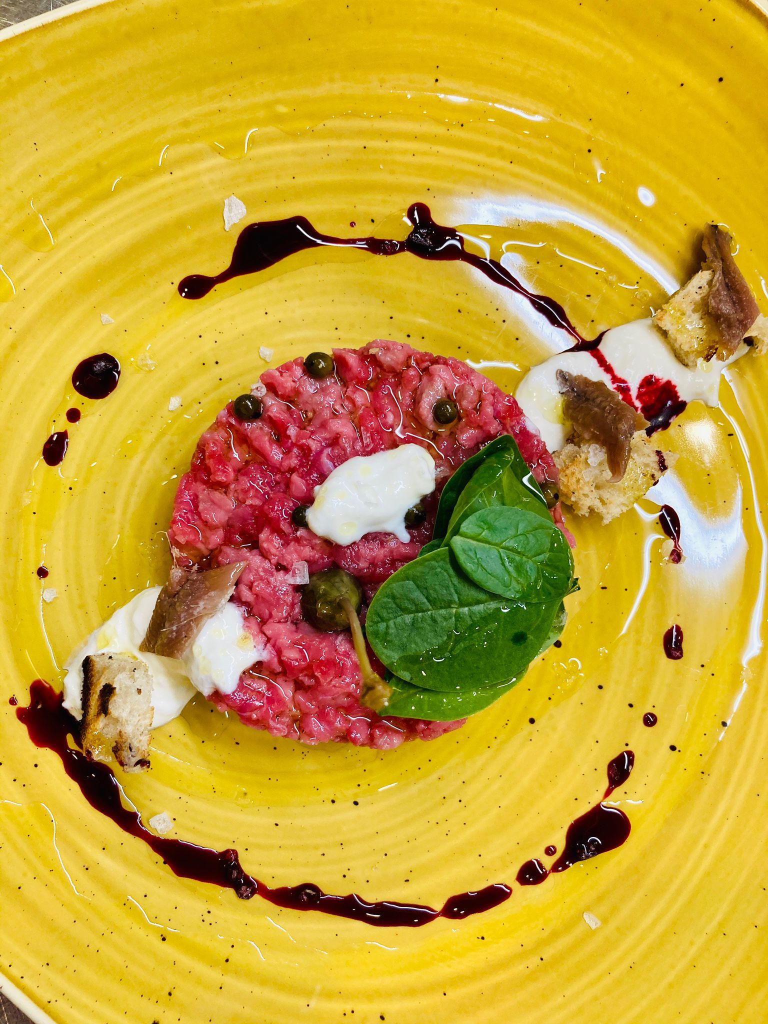 Tartare di manzo con capperi, menta e glassa balsamica su un piatto giallo.