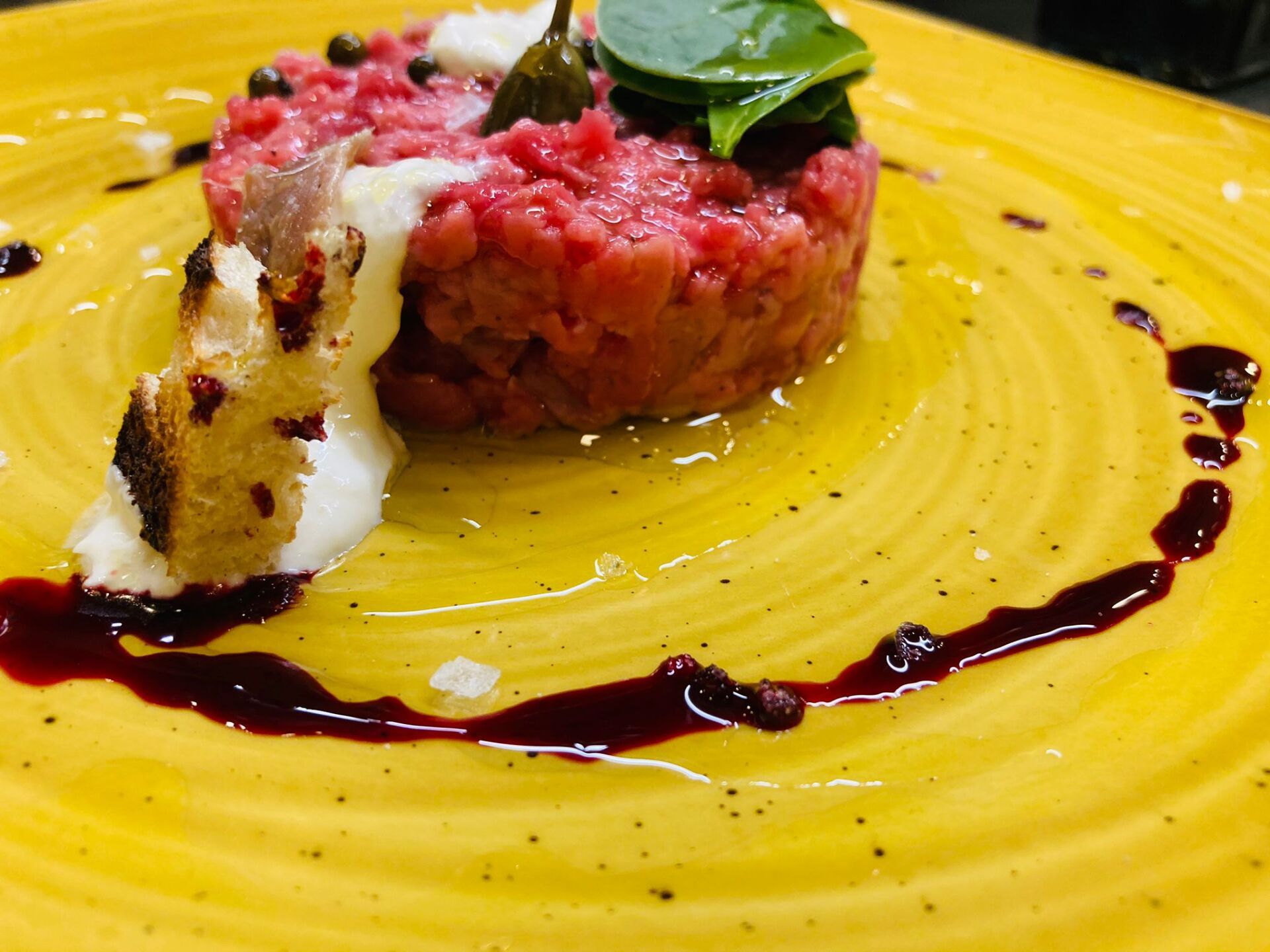 Tartare di manzo con contorno su un piatto giallo, condita con salsa.