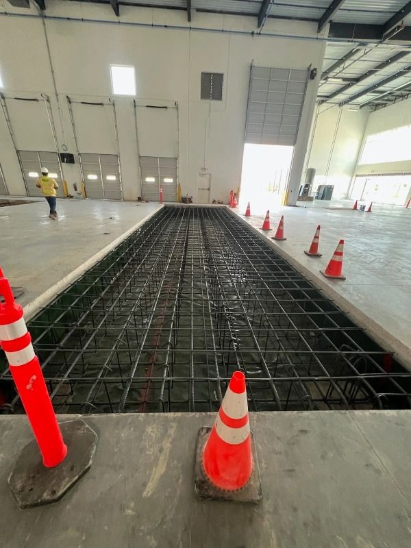 Concrete reinforcement grid in a warehouse, with orange cones and a worker in the background.