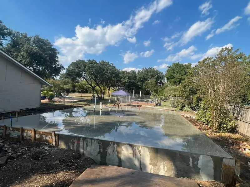 Fresh concrete foundation on a sunny day; low retaining walls with plumbing.