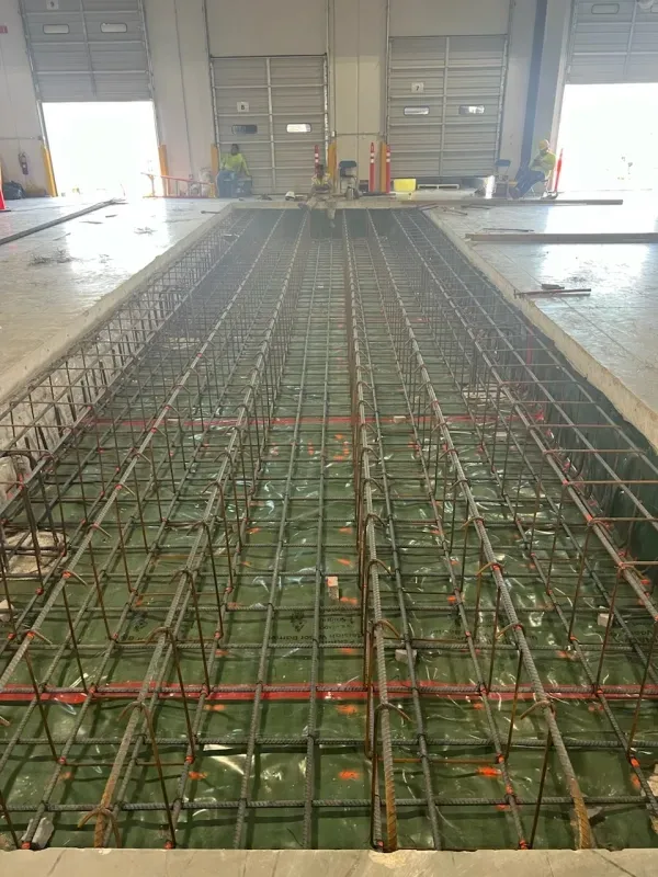 Reinforced steel framework for a concrete pour, set in a trench inside a building.