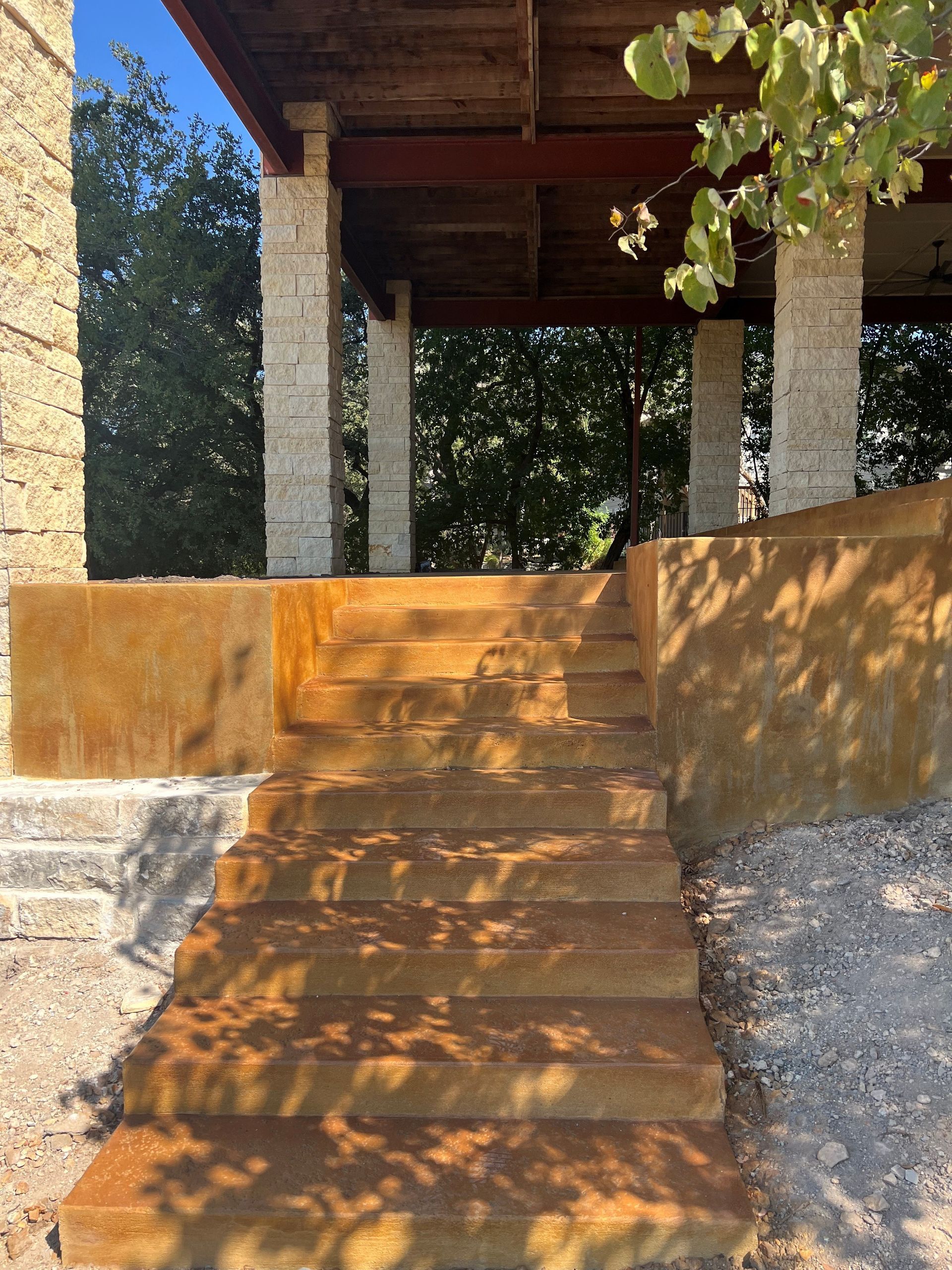 Outdoor stairs lead to a covered patio with stone columns and wood beams.