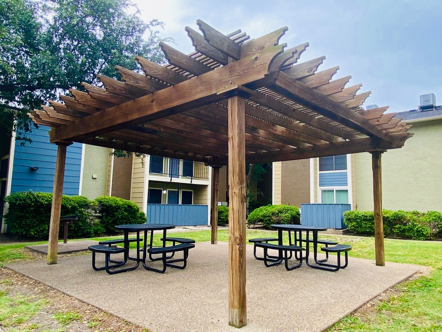 A pergola with picnic tables underneath it in a park.
