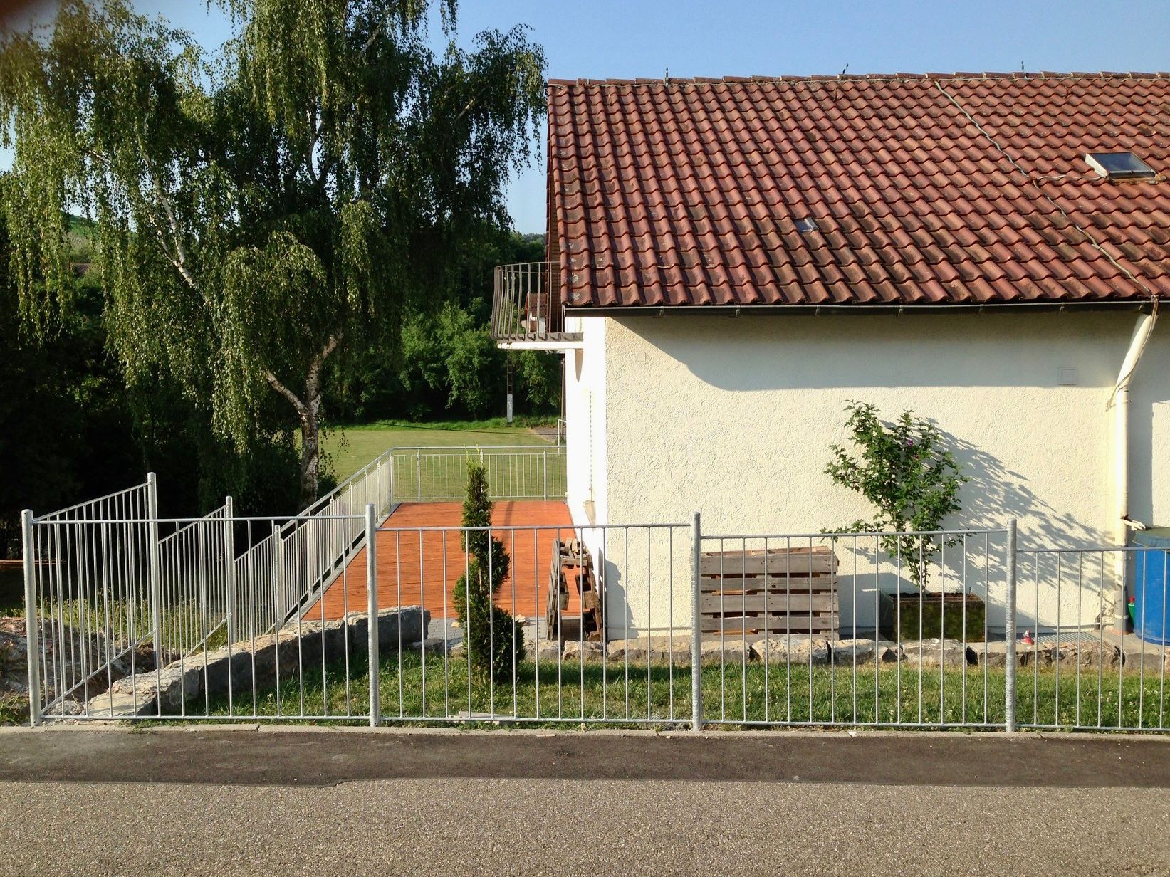 Ein weißes Haus mit einem roten Ziegeldach befindet sich hinter einem Metallzaun