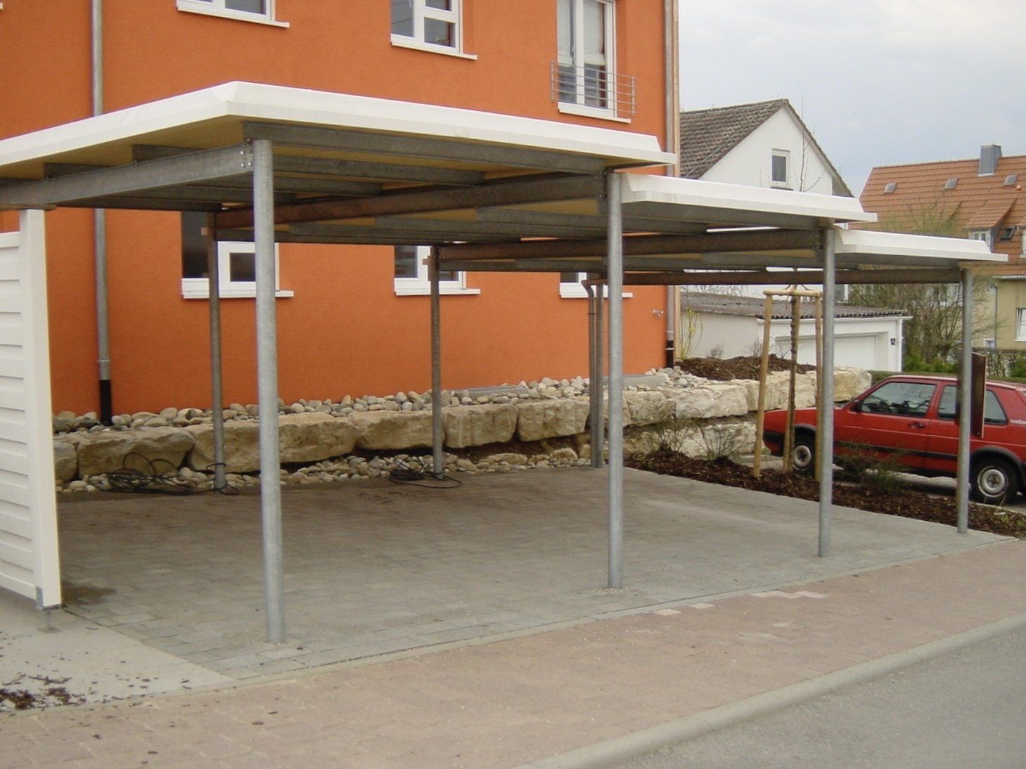 Ein rotes Auto ist unter einem Vordach vor einem orangefarbenen Gebäude geparkt