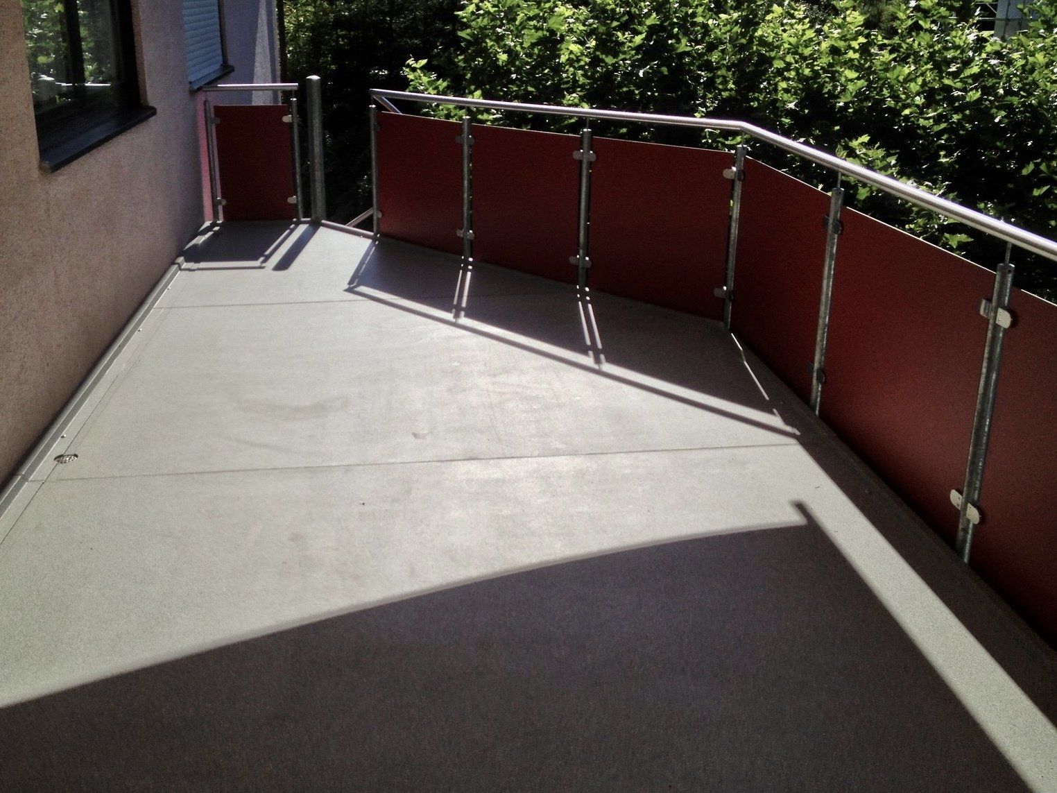 Ein Balkon mit einem roten Geländer und einem Schatten auf dem Boden