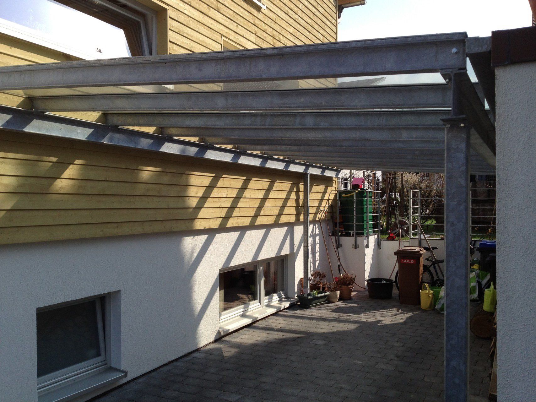 Ein Carport mit einem Vordach darüber steht neben einem Haus