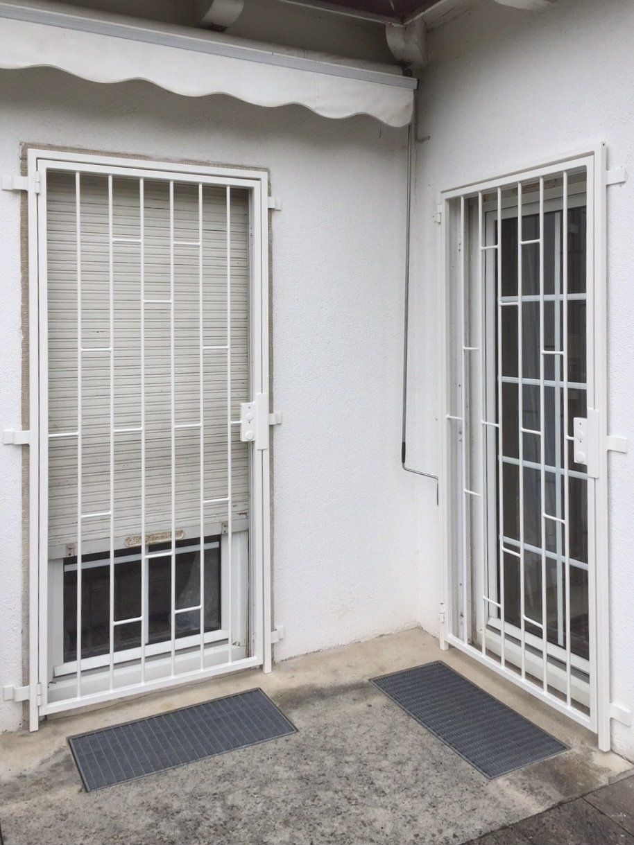 Eine weiße Tür mit einem Metallgitter und ein Fenster mit Jalousien.