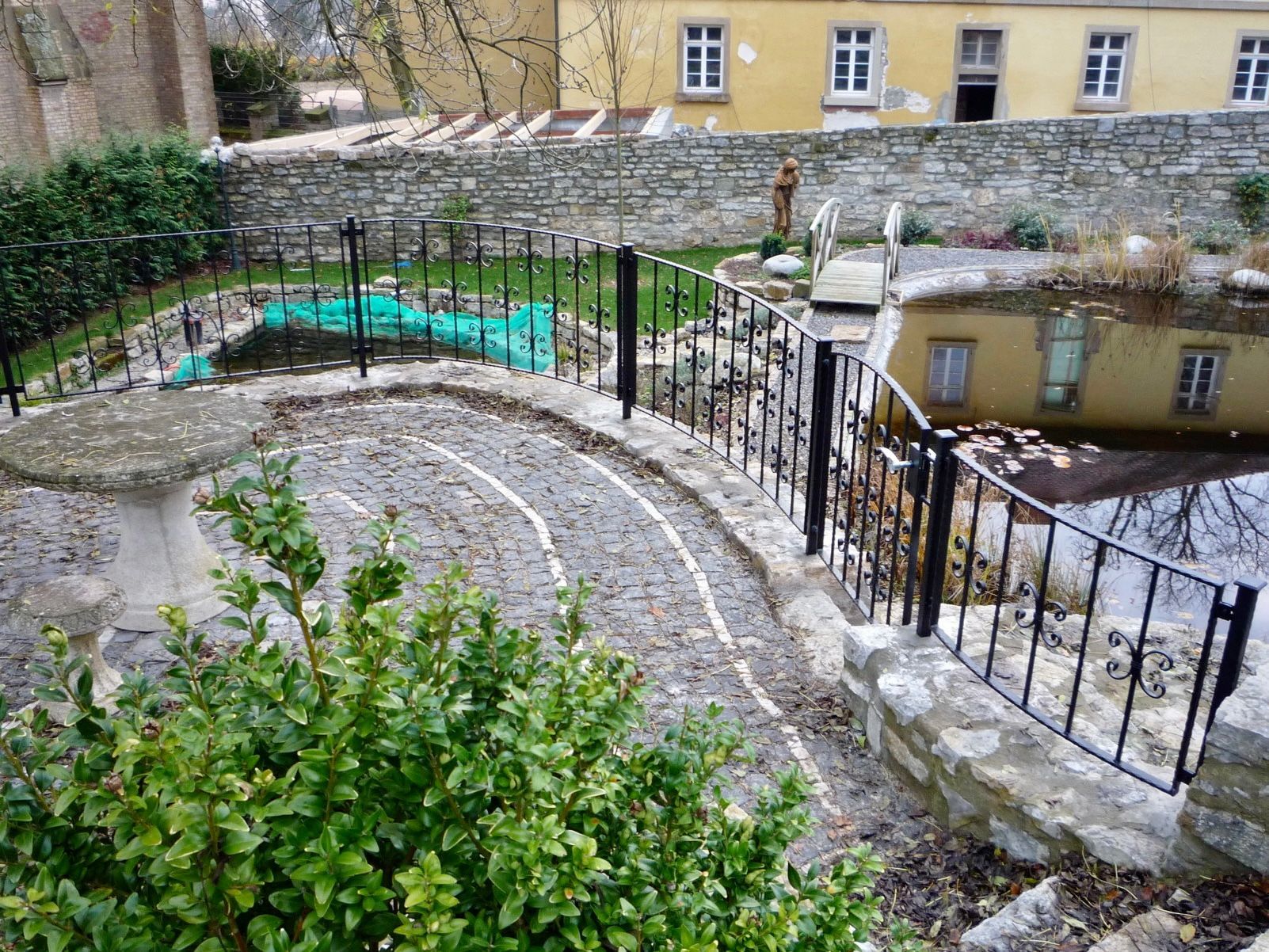 Ein Garten mit einem Zaun und einem gelben Gebäude im Hintergrund.