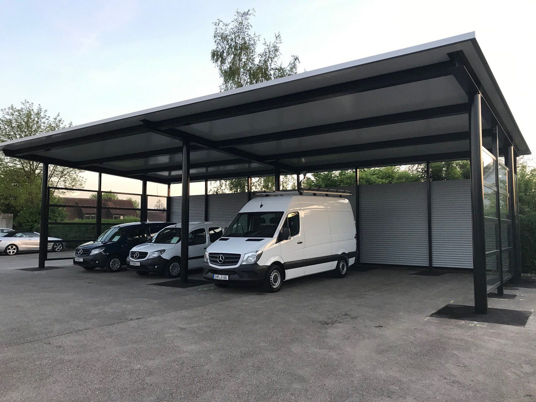 Auf einem Parkplatz steht eine Reihe Lieferwagen unter einem Vordach.