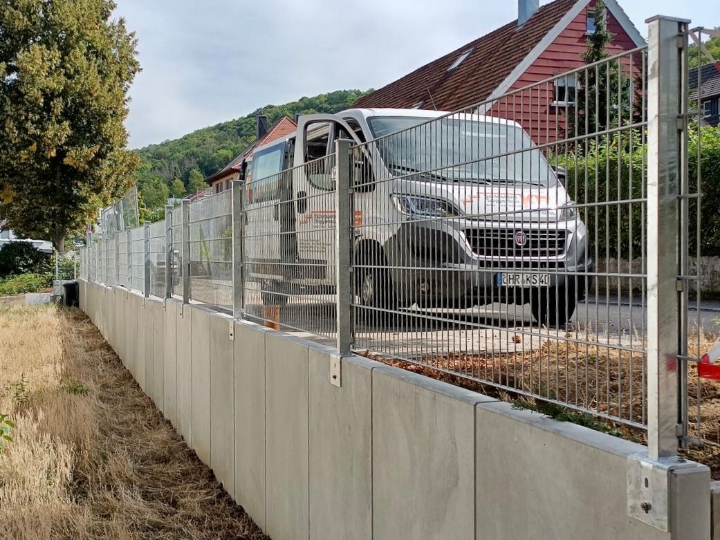 Ein weißer Lieferwagen ist hinter einem Zaun vor einem Haus geparkt.