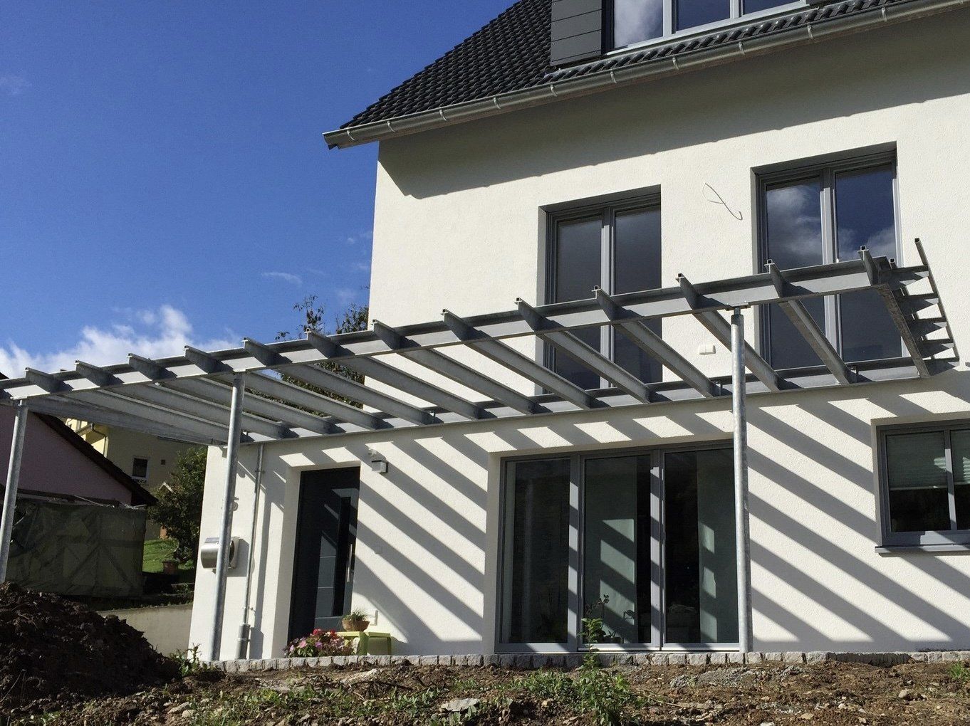 Ein weißes Haus mit einer Pergola an der Seite.