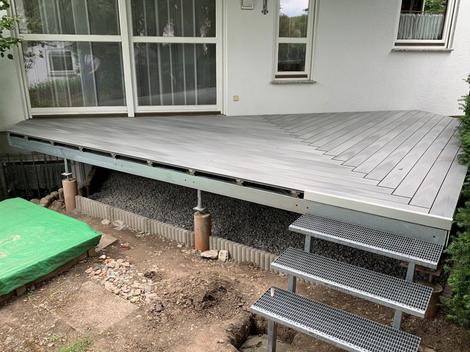 Vor einem Haus eine Holzterrasse mit einer Treppe, die hinaufführt.