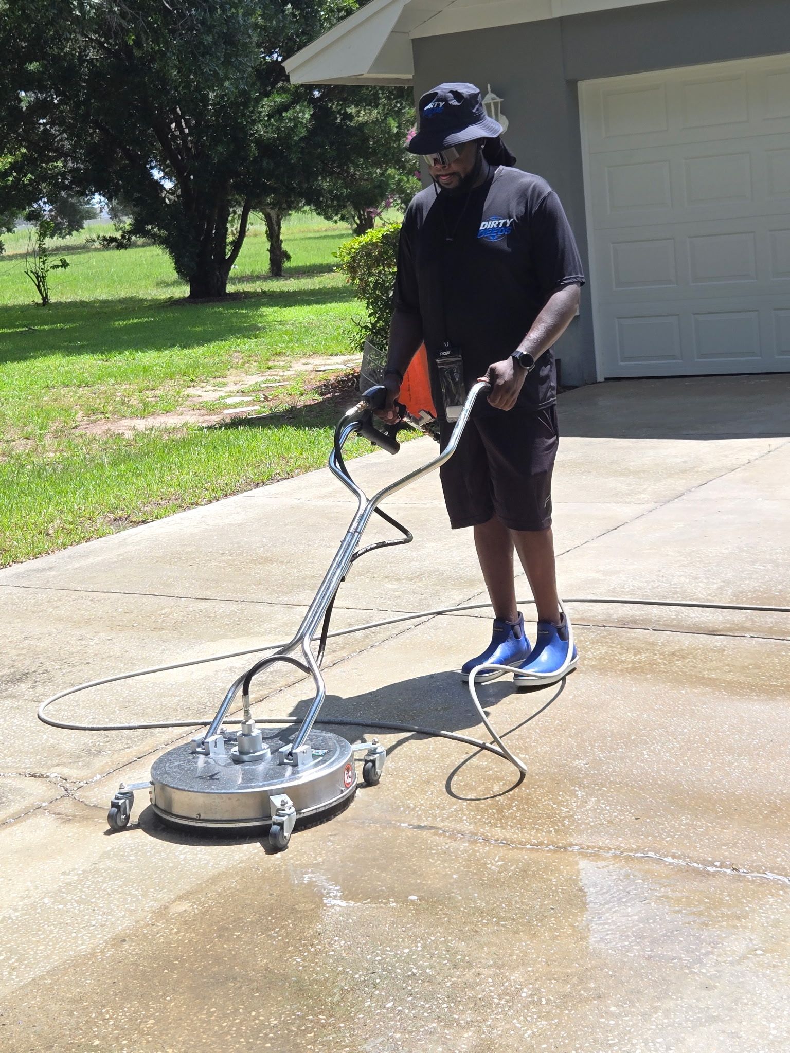 Person pressure washes a driveway beside a garage on a sunny day.