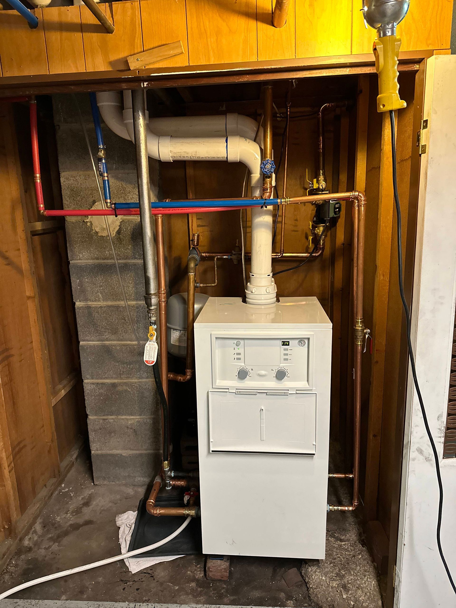 Basement utility area with white furnace, exposed pipes, and wooden joists.