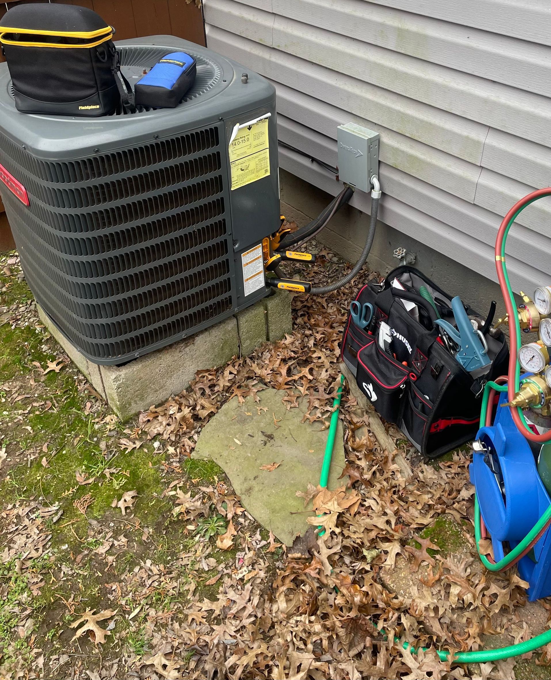 HVAC technician working on an air conditioning unit outside a building. Tools and equipment visible.