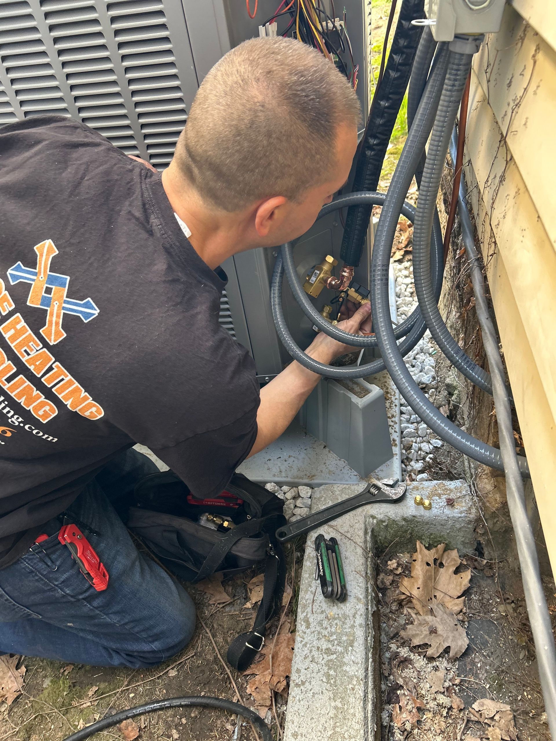 Air conditioning unit on a concrete pad, tool bag on top, set against a brick wall and grass.