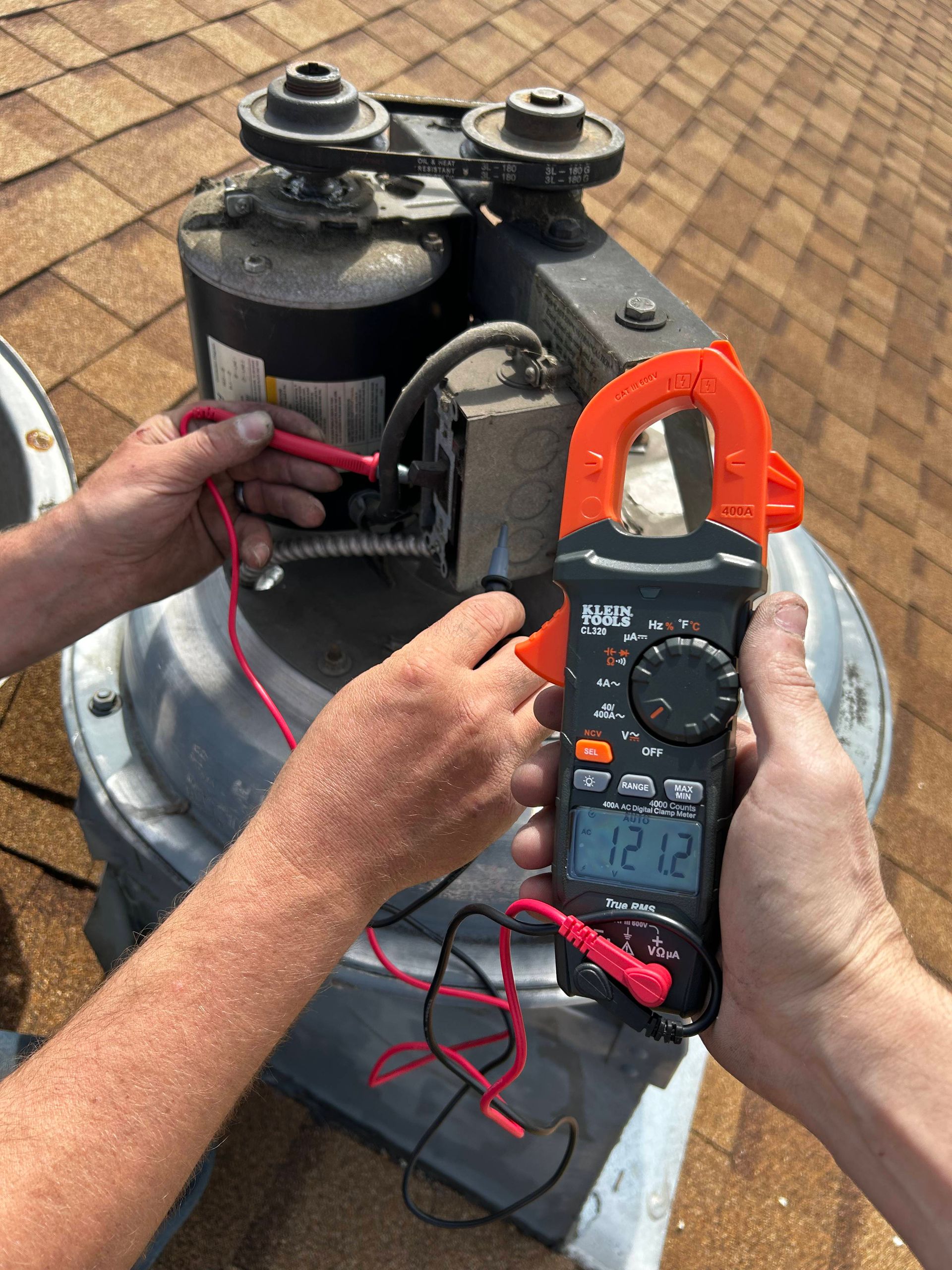 Hands using a clamp multimeter to test wiring on rooftop HVAC equipment