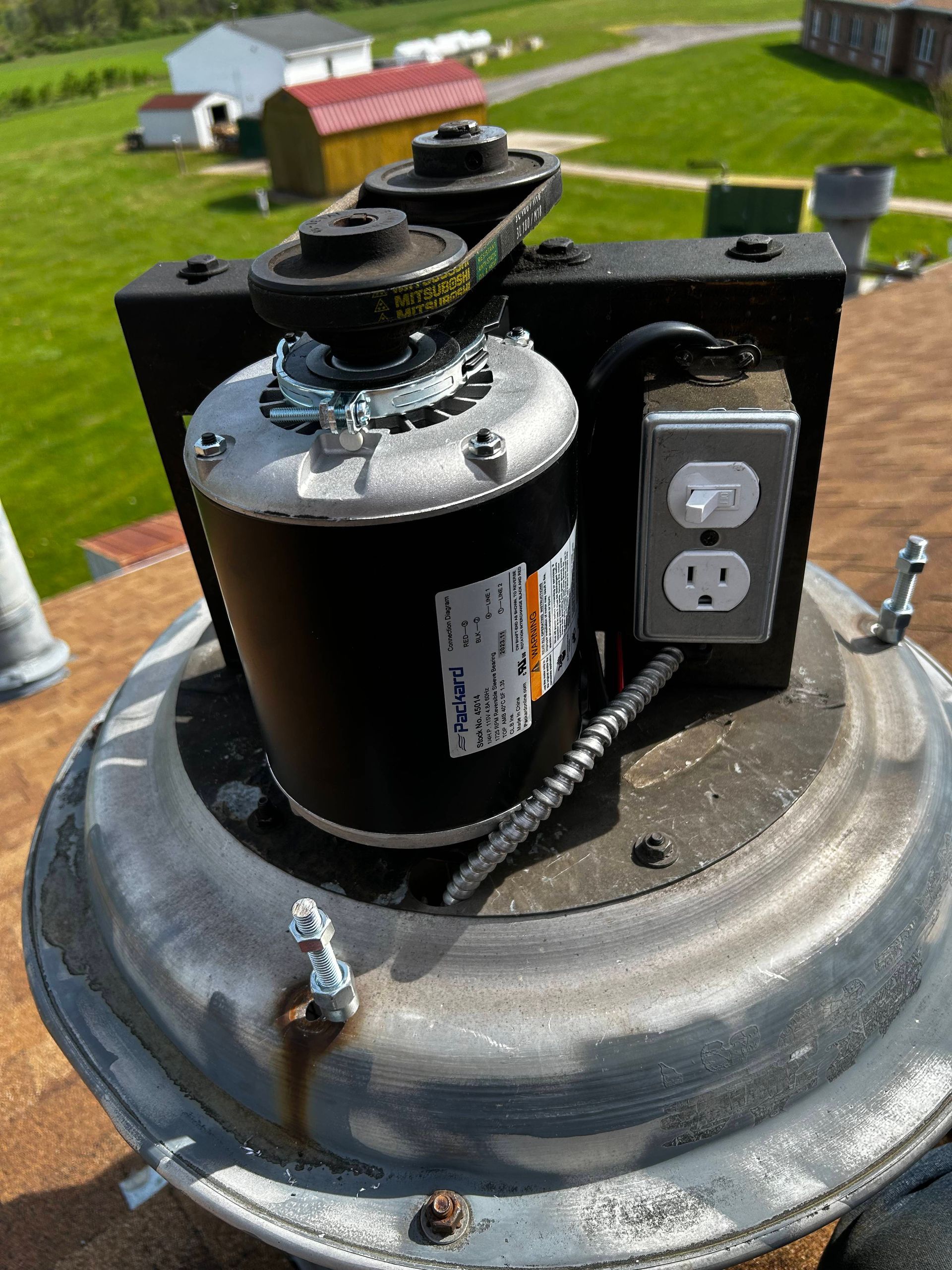 Black cylindrical electrical motor on a metal housing outdoors, with outlet panel and grassy background